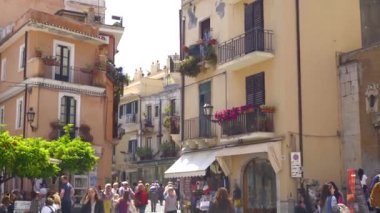 Sicilya 'da küçük Taormina kasabasının kalabalık güneşli caddesinde insanlar.