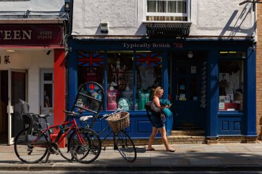 Kadın bir hediyelik eşya dükkanının önünden geçiyor ve Cambridge sokaklarında bisikletleri park ediyor.
