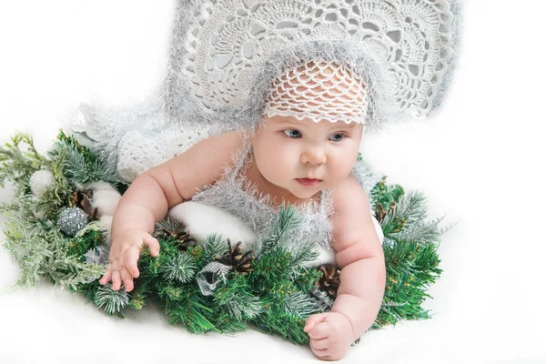 Маленькая девочка лежит на рождественском венке в белом трикотажном платье и головном уборе — стоковое фото