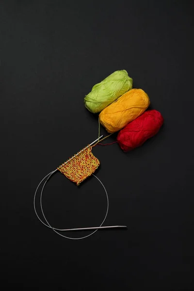 topları iplik kırmızı yeşil ve sarı siyah bir arka plan ve örgü iğneleri dikey