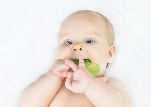 Beyaz bir yatakta yatarken bir oyuncak bir çocuk çiğniyor