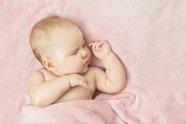 Un niño pequeño duerme en una cama debajo de una manta rosa — Foto de Stock