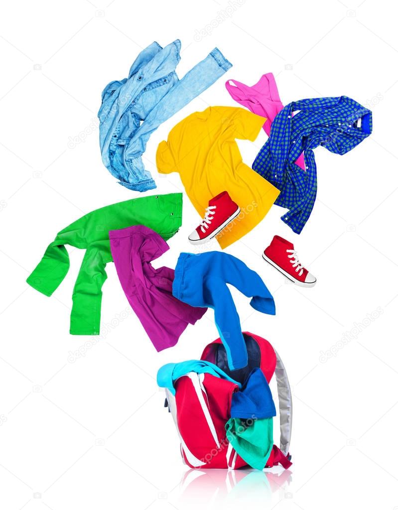 Colorful clothes are falling in a red backpack on a white backgr
