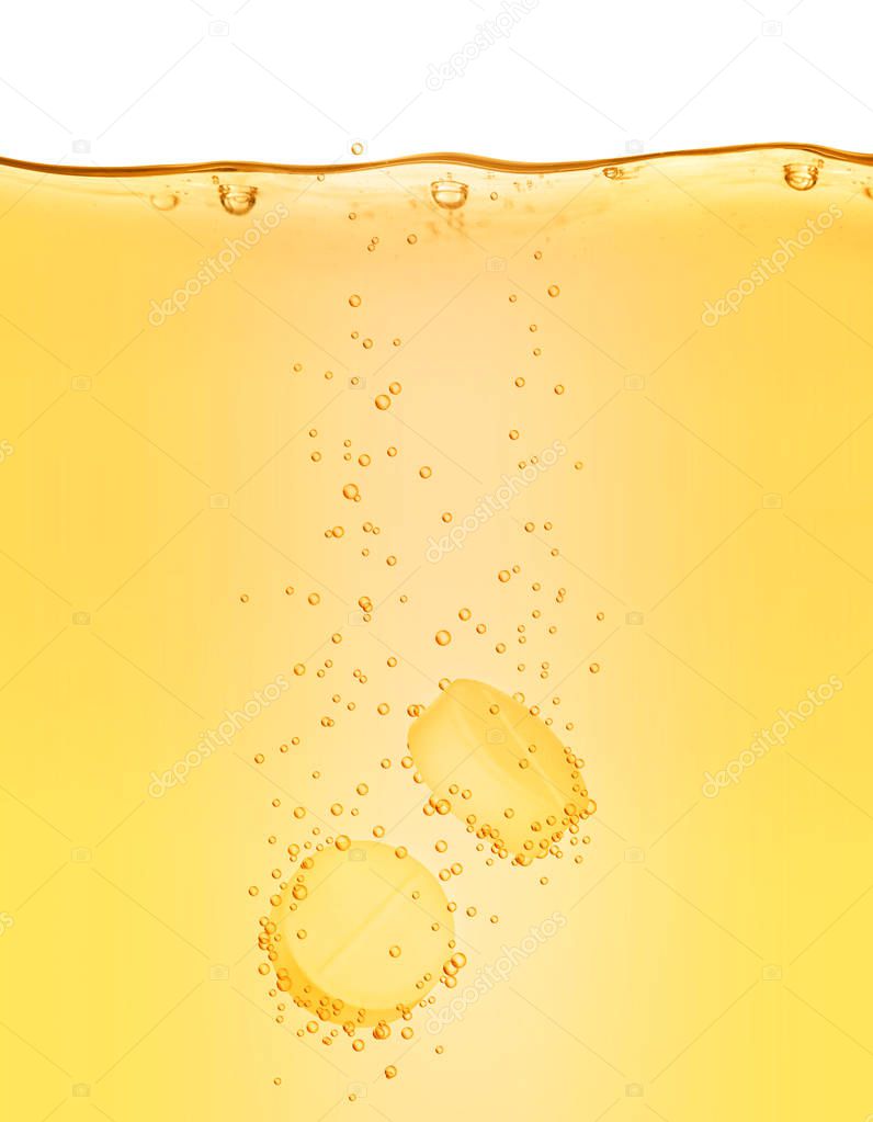 Two vitamins pills dissolves in yellow water close-up on white 