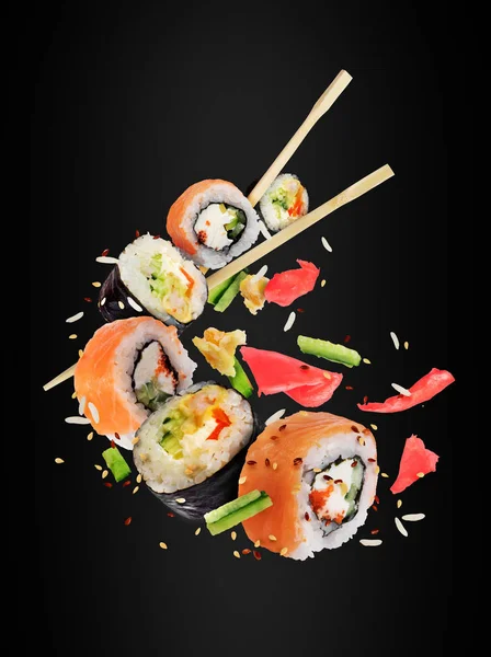 不同的新鲜寿司卷与筷子冻结在空气中黑色背景 — 图库照片