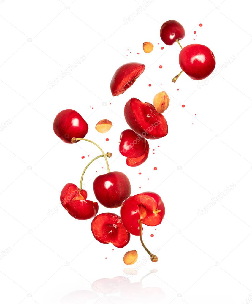 Whole and sliced fresh cherries in the air with reflection, isolated on a white background