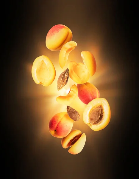 Ganze und in Scheiben geschnittene frische Aprikosen in der Luft mit einem Lichtblitz in der Dunkelheit — Stockfoto