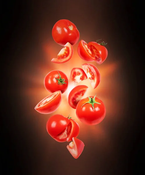 Ganze und in Scheiben geschnittene frische Tomaten in der Luft mit Lichtblitz in der Dunkelheit — Stockfoto