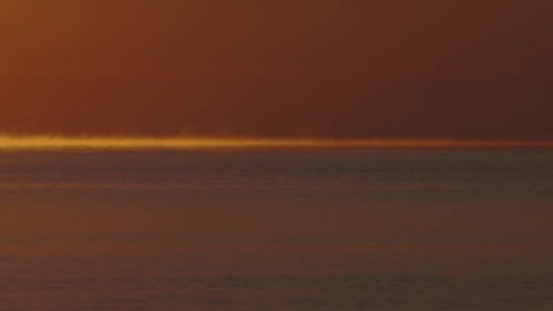 Orangefarbene Morgendämmerung, Nebel über dem Meer vor dem Hintergrund der Küste und Bäume. — Stockvideo