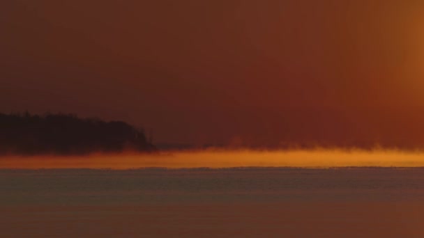 Oranje dageraad, mist boven de zee op de achtergrond van de kust en bomen. — Stockvideo