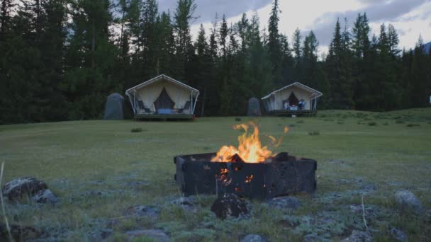 Un fuoco brucia sullo sfondo di un campeggio nella foresta sullo sfondo di montagne innevate 4K — Video Stock