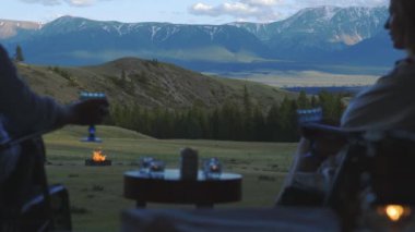 Bir kadın ve bir erkek Chalet 'lerinin balkonunda güzel bir dağ manzaralı şarap içiyorlar, ateş yanıyor. 4k