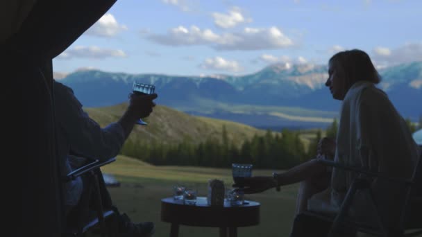 Una mujer en cuadros está bebiendo vino en el balcón con un hombre hablando. Hermosas vistas de las montañas. 4K — Vídeos de Stock