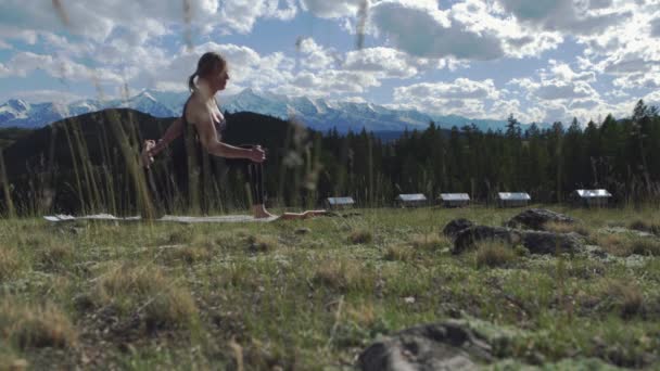 A young girl is doing yoga on the grass in the open air against the background of snow-capped mountains. 4k — 비디오