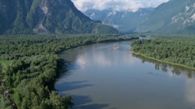 Flying over a river that flows into a lake against the backdrop of mountains 4k