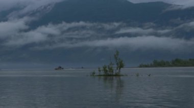 Motorlu tekne nehirde yüzer sislerin içinde dağların arkasında