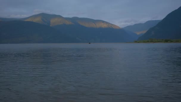 Rzeka o zachodzie słońca na tle gór. łódź pływa w oddali — Wideo stockowe
