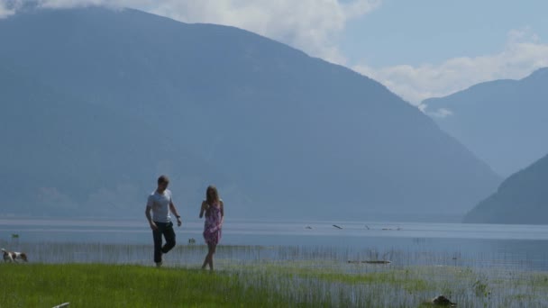 Um cara e uma garota caminham ao longo da margem do rio com seu cachorro — Vídeo de Stock