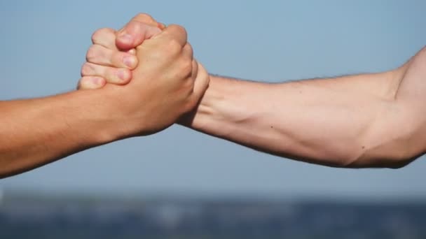 青い空を背景に 2 つの認識できない筋白人男性の友好的な握手。屋外男性腕の揺れ。外の固い握手を持つ 2 つの強い男性。チームワークと友情。クローズ アップ. — ストック動画