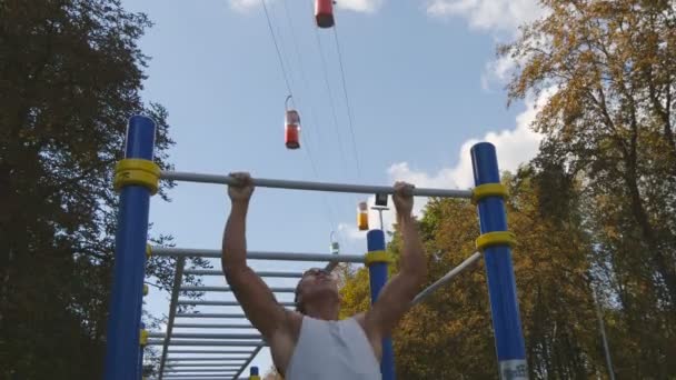 Ισχυρή μυώδης άνδρας κάνει pull ups σε ένα πάρκο. Νεαρός αθλητής πάνε πηγούνι-ups και εκτελεί ασκήσεις σε εξωτερικές οριζόντιες γραμμές. Γυμναστήριο μυώδης άνδρας εκπαίδευση έξω από το καλοκαίρι. Προπόνηση αθλητικό τρόπο ζωής — Αρχείο Βίντεο