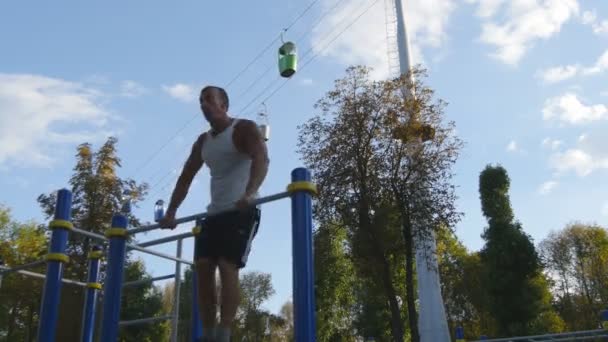 Strong muscular man doing muscle ups in a park. Young athlete doing chin-ups on horizontal bars outdoor. Fitness muscular man training outside in summer. Sportsman pulling up. Workout sport lifestyle — Stock Video