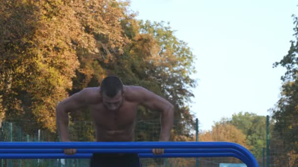 Homem atlético fazendo flexões em bares paralelos em campo de esportes no parque da cidade. Forte jovem musculoso treinamento cara ao ar livre no verão. Atleta se exercitando no playground. Exercício estilo de vida saudável. Fechar. — Vídeo de Stock