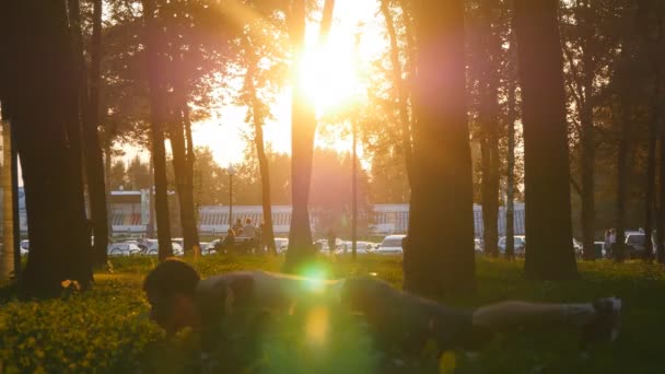 夕暮れ時の公園で若い男トレーニング。オスの運動選手が腕立て伏せジャンプ屋外 ups。背景の美しい日の出と訓練外スポーツマンのクローズ アップ。健康的なアクティブなライフ スタイル — ストック動画