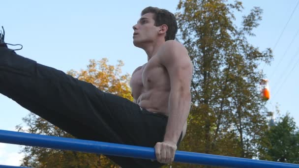 Hombre atlético ejercitar los abdominales en el bar en el parque de la ciudad. Hombre deportista realiza ejercicios de fuerza durante el entrenamiento. Chico joven demuestra ejercicio estático. Movimiento lento — Vídeo de stock