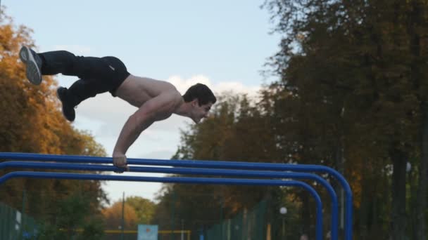 Hombre atlético haciendo elementos de gimnasia en el bar en el parque de la ciudad. Hombre deportista realiza ejercicios de fuerza durante el entrenamiento al aire libre. Chico joven demuestra ejercicio estático. Entrenamiento afuera. Movimiento lento — Vídeo de stock