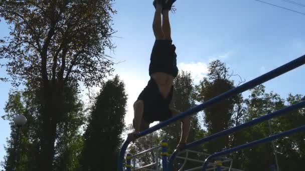 Stark muskulös man gör en handstand i en park. Passar muskulös manliga fitness killen gör stunts på räck utomhus. Atlet utbildning utför en handstand muskler utanför. Träning sport livsstil — Stockvideo