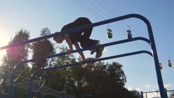 Hombre atlético haciendo elementos de gimnasia en el bar en el parque de la ciudad. Hombre deportista realiza ejercicios de fuerza durante el entrenamiento al aire libre. Chico joven demuestra ejercicio estático. Estilo de vida saludable — Vídeos de Stock