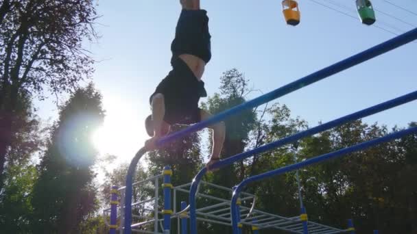 Sterke gespierde man doet een handstand in een park. Fit gespierde mannelijke fitness kerel stunts op horizontale balken buiten doen. Atleet opleiding voert een handstand op spier buiten. Training sport levensstijl — Stockvideo