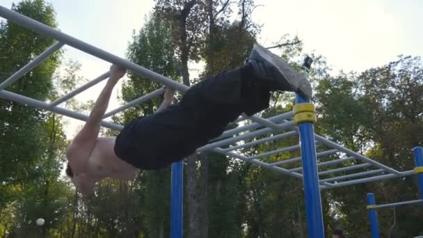 Homem atlético fazendo elementos de ginástica no bar horizontal no parque da cidade. Esportista masculino realiza exercícios de força durante o treino ao ar livre. Jovem demonstra exercício estático. Formação fora — Vídeo de Stock