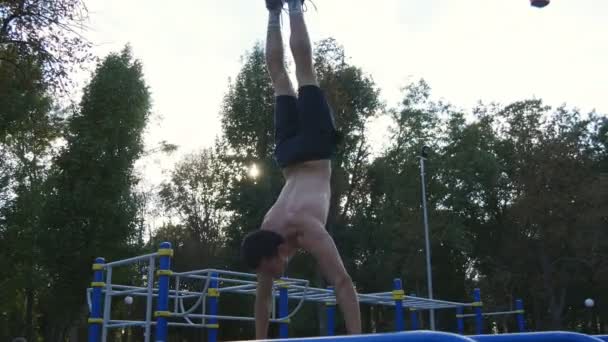 Forte homem musculoso fazendo um suporte de mão em um parque. Apto musculoso homem fitness cara fazendo acrobacias em barras horizontais ao ar livre. Treinamento atleta executa um suporte de mão no músculo fora. Estilo de vida desportivo treino — Vídeo de Stock