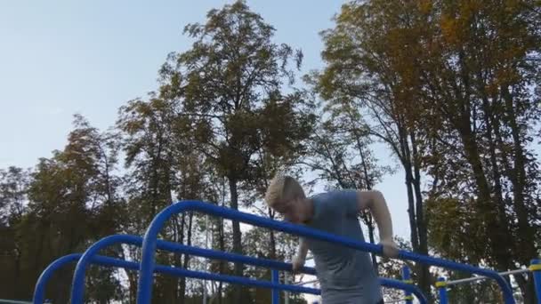 Hombre atlético haciendo flexiones en bares paralelos en el campo de deportes en el parque de la ciudad. Fuerte joven musculoso entrenamiento al aire libre en verano. Atleta haciendo ejercicio en el patio de recreo. Ejercicio estilo de vida saludable. Primer plano. — Vídeos de Stock