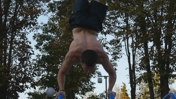 Erős, izmos ember csinálás egy parkban kézen. Izmos férfi fitness srác csinál stunts vízszintes sávok szabadtéri illik. Sportoló képzés kézen az izom kívül végzi. Lassú mozgás — Stock videók