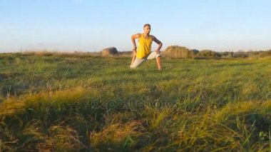 Çayır ve yoga egzersiz yaparak yeşil çim oturan genç adam. Doğa vücudu germe kas adam. Güneşli gün açık eğitim. Arka plan, güzel manzara. Yakın çekim