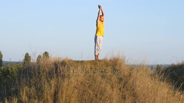 Caucasiano praticando movimentos de ioga e posições na natureza. Jovem desportivo em pé no ioga pose ao ar livre. Equilibração de atletas. Bela paisagem como fundo. Estilo de vida ativo saudável — Vídeo de Stock