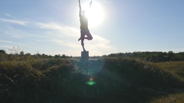 Silueta de hombre deportivo de pie en la pose de yoga al aire libre. Yogui practicando movimientos de yoga y posiciones en la naturaleza. Atleta balanceándose en una pierna. Hermoso cielo y sol como fondo. Vida activa saludable — Vídeos de Stock