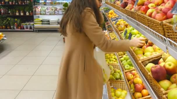 Mujer seleccionando manzanas rojas frescas en el departamento de productos de comestibles y poniéndolo en una bolsa de plástico. Chica bonita joven está eligiendo manzanas en el supermercado y ponerlos en la cesta de la tienda. De cerca. — Vídeos de Stock