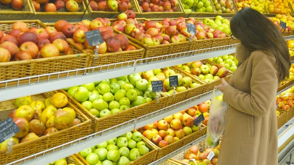 Женщина выбирает свежие красные яблоки в продуктовом отделе и кладет их в пластиковый пакет. Молодая красивая девушка выбирает яблоки в супермаркете и положить их в корзину магазина. Закрыть — стоковое фото