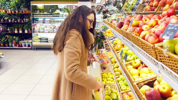 Woman selecting fresh red apples in grocery store produce department and putting it in plastic bag. Young pretty girl is choosing apples in supermarket and putting them into shop basket. Close up