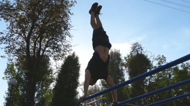 Güçlü kas adam amuda bir parkta. Kaslı erkek spor adamı yatay çubuklarında açık stunts yapıyor. Sporcu eğitim kas dışında bir hareketten gerçekleştirir. Egzersiz spor yaşam tarzı