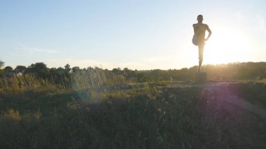 Yogi Yoga uygulamak hareket eder ve doğal olarak konumlandırır. Sportif adam poz yoga açık ayakta silüeti. Tek ayak üstünde Dengeleme atlet. Güzel gökyüzü ve güneş arka plan olarak. Sağlıklı aktif yaşam tarzı