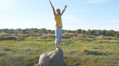 Yoga poz açık taşına ayakta sportif delikanlı. Yogi Yoga uygulamak hareket eder ve doğal olarak konumlandırır. Tek ayak üstünde Dengeleme atlet. Güzel manzara arka plan olarak. Sağlıklı aktif yaşam tarzı