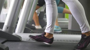 Kadın bacaklar yürüyüş ve spor salonunda koşu bandı üzerinde çalışan. Kardiyo egzersiz sırasında egzersiz genç kadın. Spor ayakkabıları eğitim kapalı spor kulübünde kız ayak. İnsanlar koşuyor. Yakın çekim