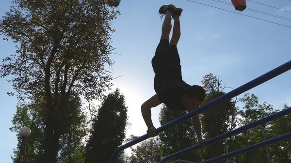 Sterke gespierde man doet een handstand in een park. Fit gespierde mannelijke fitness kerel stunts op horizontale balken buiten doen. Atleet opleiding voert een handstand op spier buiten. Training sport levensstijl — Stockfoto