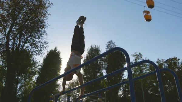 Sterke gespierde man doet een handstand in een park. Fit gespierde mannelijke fitness kerel stunts op horizontale balken buiten doen. Atleet opleiding voert een handstand op spier buiten. Training sport levensstijl — Stockfoto