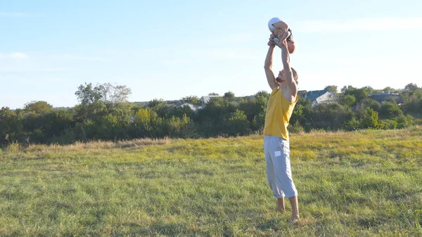 El joven padre vomitando a su pequeño hijo al aire libre. Papá jugando con su hijo en la naturaleza. Feliz familia pasando tiempo juntos afuera en el prado. Hermoso paisaje de fondo. De cerca. — Foto de Stock