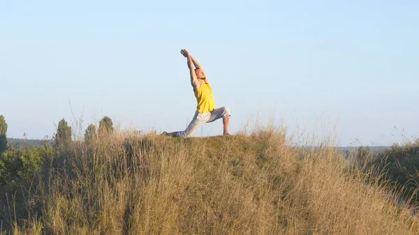 Kaukasische guy beoefenen van yoga beweegt en posities in de natuur. Sportieve jongeman permanent op yoga pose buiten. Atleet balanceren. Mooi landschap als achtergrond. Gezonde actieve levensstijl — Stockfoto